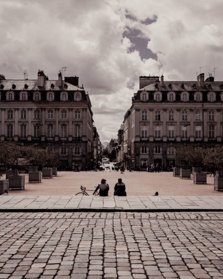 two person sitting on pathway beside beige and white concrete building under white skies