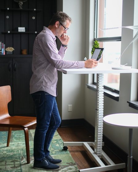 man in gray dress shirt and blue denim jeans standing beside white table